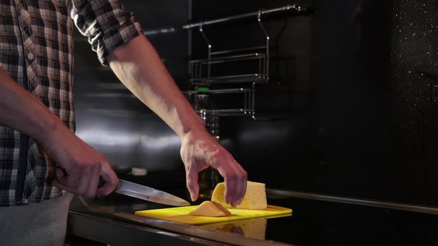 Man cuts cheese with a knife on a cutting board