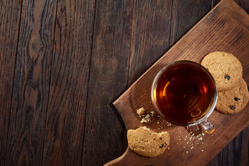 Cup of tea with cookies on a cutting board on a wooden background, top view