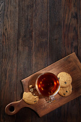 Cup of tea with cookies on a cutting board on a wooden background, top view