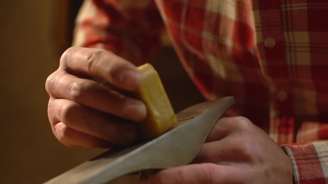 Closeup view of male master doing carpentry on furniture manufacture, and polishing wooden detail with soap slow motion