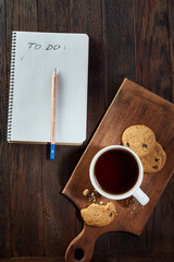 Cup of tea with cookies, workbook and a pencil on a wooden background, top view
