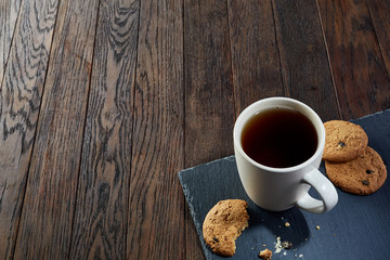 Cup of tea with cookies, workbook and a pencil on a wooden background, top view