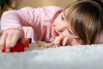 Obraz na płótnie Canvas Kid with down syndrome playing with toy cubes while lying on a floor