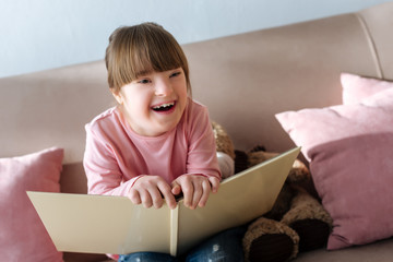 Kid with down syndrome holding book and laughing