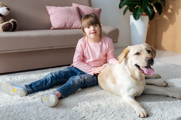 Kid with down syndrome sitting on the floor with Labrador retriever on carpet