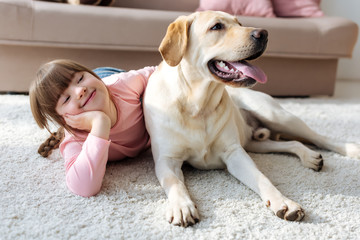 Happy child with down syndrome lying on the floor with Labrador retriever