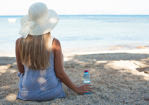 Beautiful young woman sitting on the beach and holding bottle of water