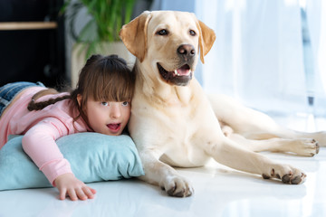 Kid with down syndrome lying on the floor next to Labrador retriever dog