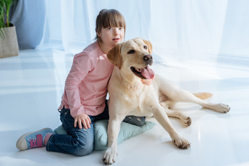 Child with down syndrome near Labrador dog on the floor