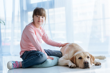 Child with down syndrome sitting on the floor with Labrador retriever