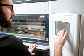 Man operating offset machine pushing touch screen at the printing manufacturing. Close-up view