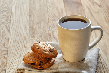 Porcelain teacup with chocolate chips cookies on cotton napkin on a rustic wooden background, top view