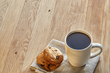 Porcelain teacup with chocolate chips cookies on cotton napkin on a rustic wooden background, top view