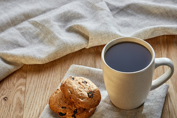 Porcelain teacup with chocolate chips cookies on cotton napkin on a rustic wooden background, top view