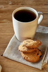 Porcelain teacup with chocolate chips cookies on cotton napkin on a rustic wooden background, top view
