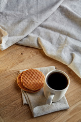 Porcelain teacup with waffles on cotton napkin on a rustic wooden background, top view, vertical