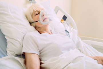 Obraz na płótnie Canvas Recovery process. Senior lady sleeping gin a hospital bed and wearing a respiratory support mask while undergoing treatment.