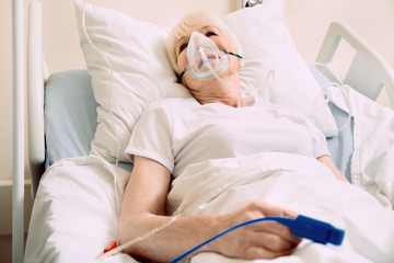 Obraz premium Staying in a good mood. Positive minded senior lady smiling while lying in a hospital bed with an oxygen mask and a pulse oximeter.