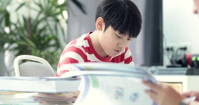 Serious Asian mother with son doing homework in the living room. Mom teaches son how to genius.