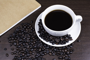 Black coffee in cup and coffee bean and book on wood background.