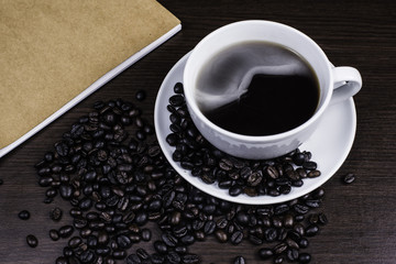 Black coffee in cup and coffee bean and book on wood background.