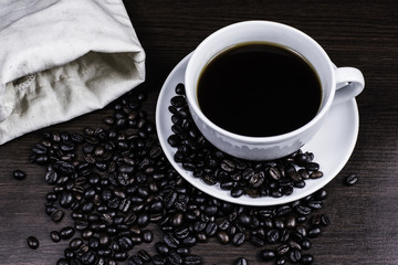 Black coffee in cup and coffee bean and bag on wood background.