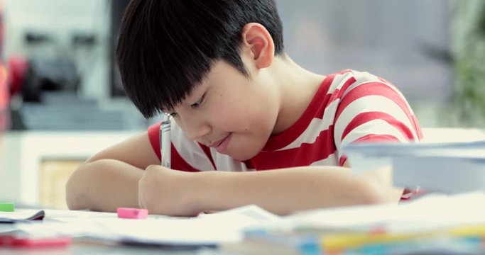 Serious asian boy doing your homework at home.