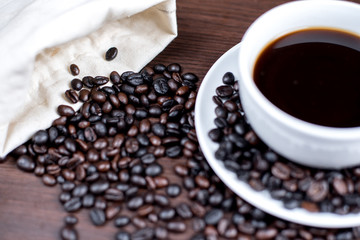 Black coffee in cup and coffee bean and bag on wood background.