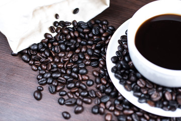 Black coffee in cup and coffee bean and bag on wood background.
