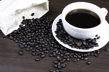 Black coffee in cup and coffee bean and bag on wood background.