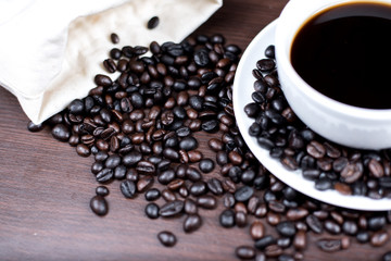 Black coffee in cup and coffee bean and bag on wood background.