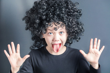 Beautiful girl in a black curly wig raised her hands up and tongue out
