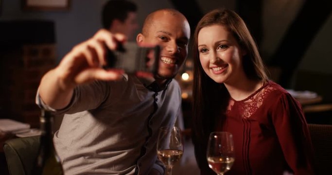 4K Attractive mixed ethnicity couple drinking wine in a bar pose to take a selfie with smartphone. Slow motion.