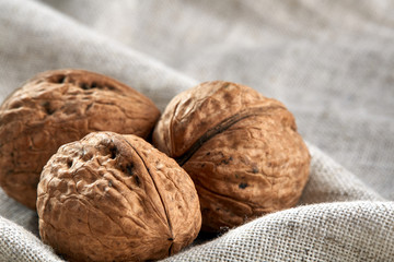A stack of hard shells of walnuts piled together on light grey fabric cotton tablecloth, selective focus