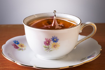 Drop falling into a cup full of tea on a gray background