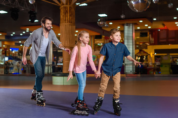 Fototapeta na wymiar father and little children skating together on roller rink
