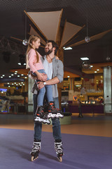 happy father holding daughter in roller skates on roller rink