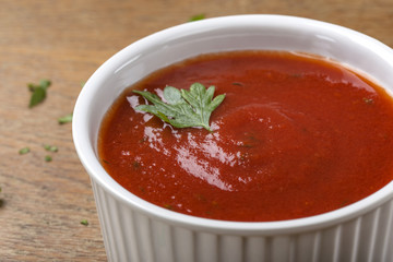 White bowl filled with homemade tomato sauce with herbs on wooden background