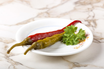 Pickled green and red peppers on plate on the table with parsley