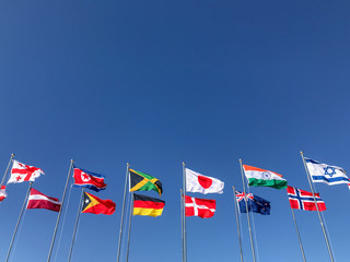 Flags of several countries waving in front of a blue sky