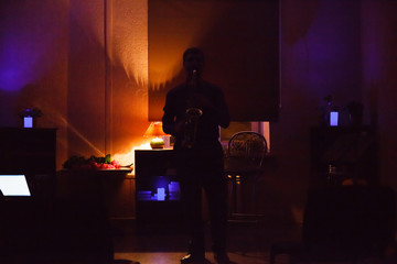 Fototapeta na wymiar Man playing on saxophone in dark room