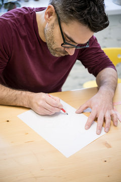 Young Designer Drawing the Sketch Using Pencil on the Wooden Table in Bright Studio
