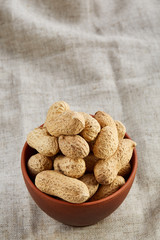 Unpeeled peanuts in ceramic bowl closeup, selective focus