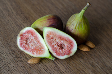 Close-up of fresh figs with one slised ripe fig and three almond nuts on a wooden table background