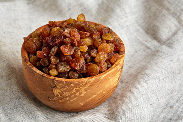 Wooden bowl with golden raisins on light tablecloth, close-up, selective focus