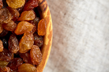 Wooden bowl with golden raisins on light tablecloth, close-up, selective focus