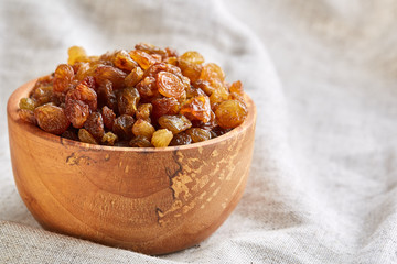 Wooden bowl with golden raisins on light tablecloth, close-up, selective focus