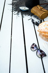 Minimal styled flat lay isolated on white wood background. Feminine desk top view with summer accessories: hat, sunglasses, vintage photo camera, handbag, shell, anchor, boat, stones, fish