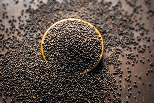 Close up of mustard seeds/Rai or brown mustard seeds in a small plate on a wooden surface in dark Gothic colors.