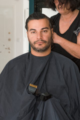 Female barber working with hair clipper, combing young man's head